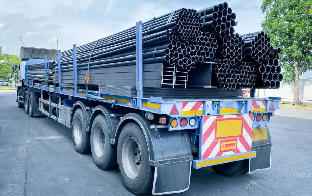 Photo of Trucks with long trailers carrying steel bars for building construction. Construction steel is ready to be delivered to the customer.
