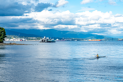 Vancouver, British Columbia - July 25, 2023: The view of Coal Harbour seaside park, a woman is playing a canoe on the water, Vancouver, Canada.