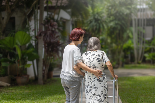 Elderly woman exercise walking in backyard with daughter.