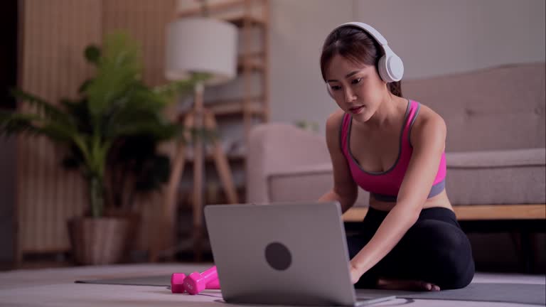 Young asian woman use laptop to listening music after watching fitness video to doing exercise