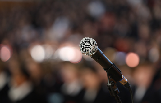 Close up of a microphone on stage with a burred bokeh audience or crowd. Public speaking performing nervousness or anxiety theme
