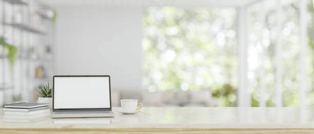 istock A white-screen laptop mockup on a white tabletop over a blurred, modern bright living room 1637189040