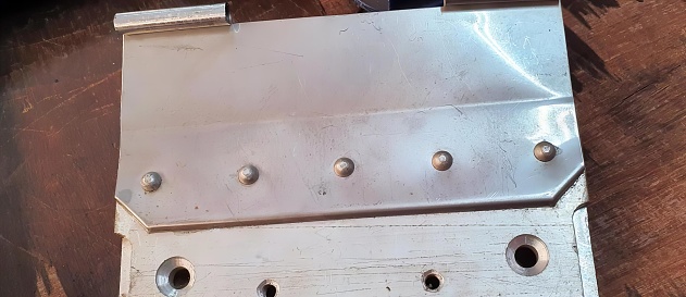 a photography of a metal plate with holes in it on a table, electrical switch plate with holes on a wooden surface.