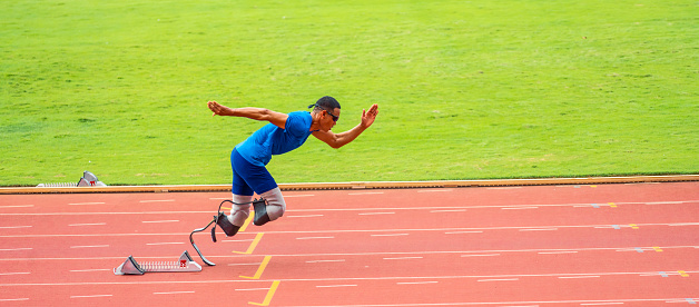 Asian para-athletes disabled with prosthetic blades running at stadium. Attractive amputee male runner exercise and practicing workout for Paralympics competition regardless of physical limitations.