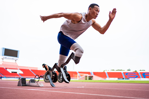 Asian para-athletes disabled with prosthetic blades running at stadium. Attractive amputee male runner exercise and practicing workout for Paralympics competition regardless of physical limitations.
