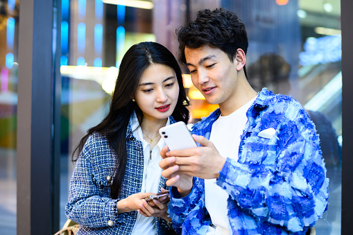 Asian young heterosexual couple using phone in city street