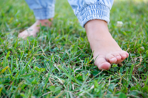 The child walks barefoot on the grass.