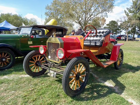 Chascomus, Argentina - Apr 15, 2023: Old red 1915 Ford Model T open runabout roadster on the lawn. Nature, green, grass and trees. Classic car show.