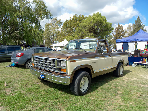 Chascomus, Argentina - Apr 15, 2023: Old white and brown 1980s Ford Ranger XLT 4x4 off road pickup truck on the lawn. Nature, grass, trees. CAACMACH 2023 classic car show.