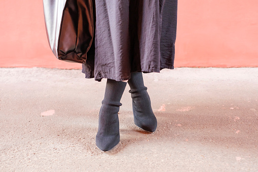 Female legs in black autumn boots against a background of concrete and a pink wall close up.