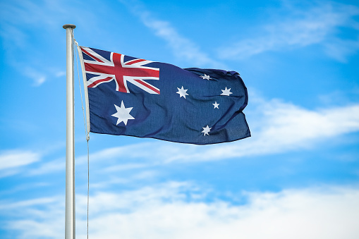 Australian flag flying on a flagpole with clouds and blue sky in the background