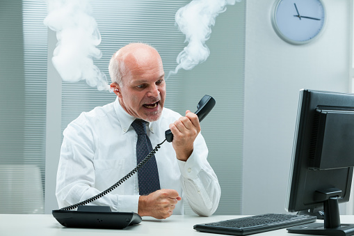 Exasperated businessman screams at someone on the phone, agitated by subpar support. So furious, it's as if smoke billows from his ears. Frustrated by these calls, personal meetings are preferred