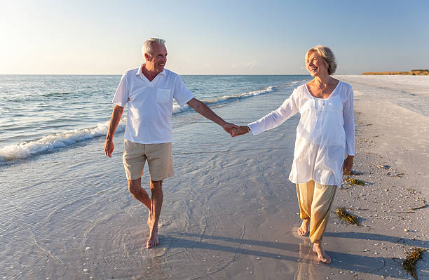 lächelnd altes paar hand in hand am strand - couple senior adult travel action stock-fotos und bilder