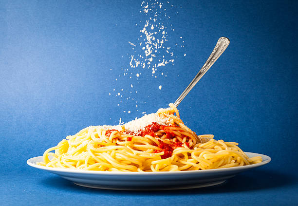 Spaghetti with simple tomato and falling Parmesan cheese on a blue background