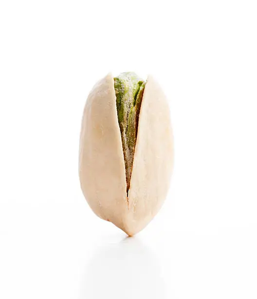 Pistachio nut shown balancing in a vertical position on a white background