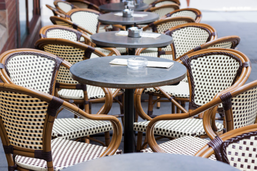 Outdoor restaurant with row of tables, ashtrays and cane chars, full frame horizontal composition