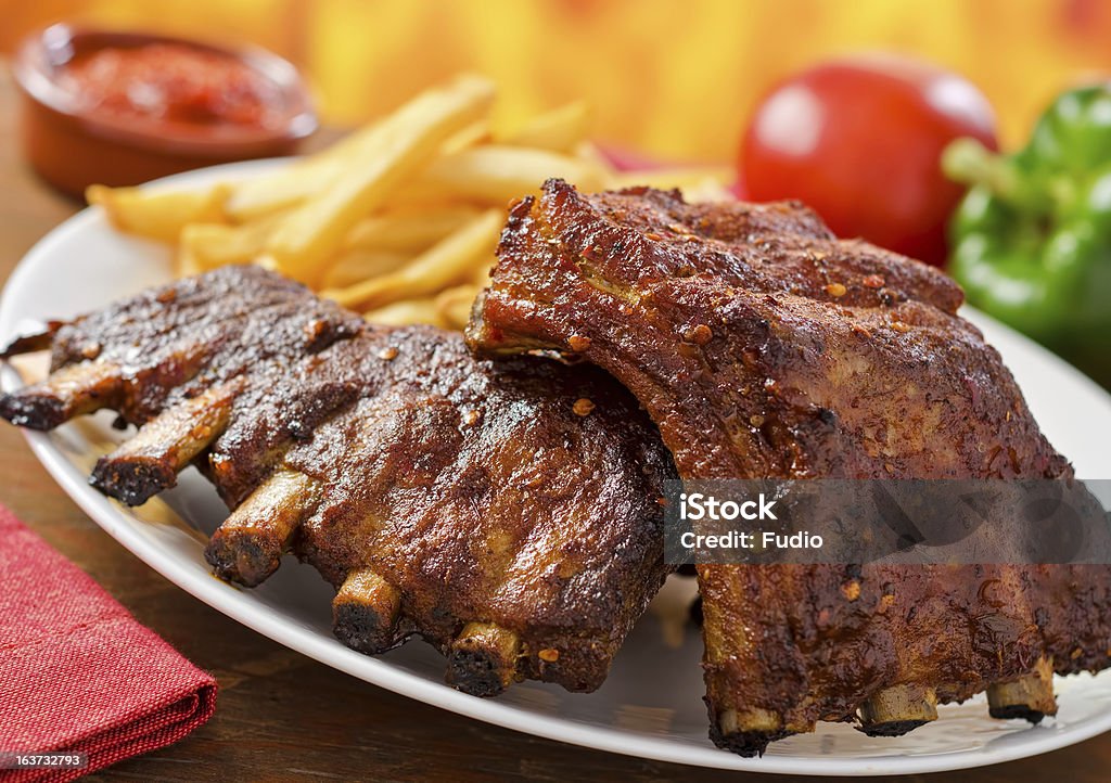 Pork Baby Back Ribs Two racks of barbecued pork baby back ribs with french fries and sauce. Barbecue - Meal Stock Photo