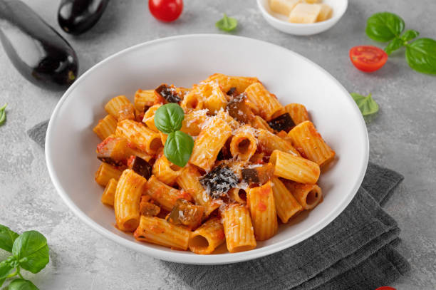 Pasta alla Norma. Italian pasta with eggplant, tomato sauce, cheese and basil in a gray concrete background. Comfort food. Pasta alla Norma. Italian pasta with eggplant, tomato sauce, cheese and basil in a gray concrete background. Comfort food tomato rigatoni stock pictures, royalty-free photos & images