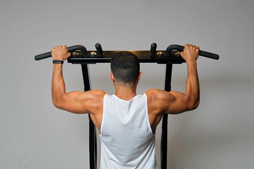Strong Hispanic man doing pull-ups at a gym.