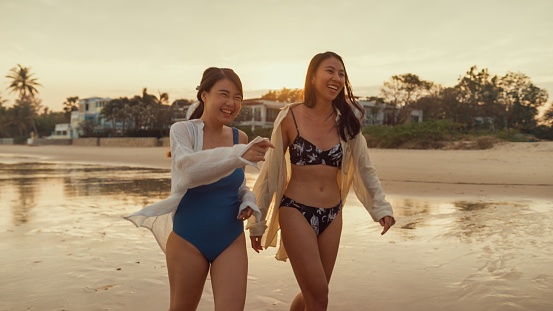 Young Asian female friends walking on tropical beach. Healthy active lifestyle and summer vacation concept.