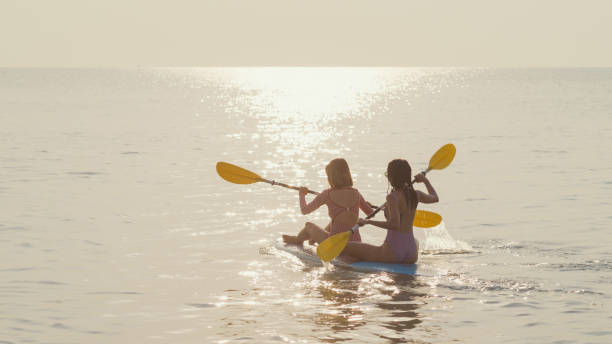 istock Young Asian female friends sitting on surfboard and using paddle while floating on water. Healthy active lifestyle and summer vacation. 1637370332