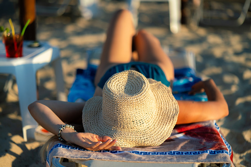 Back view of relaxed woman with straw hat spending summer day on the beach