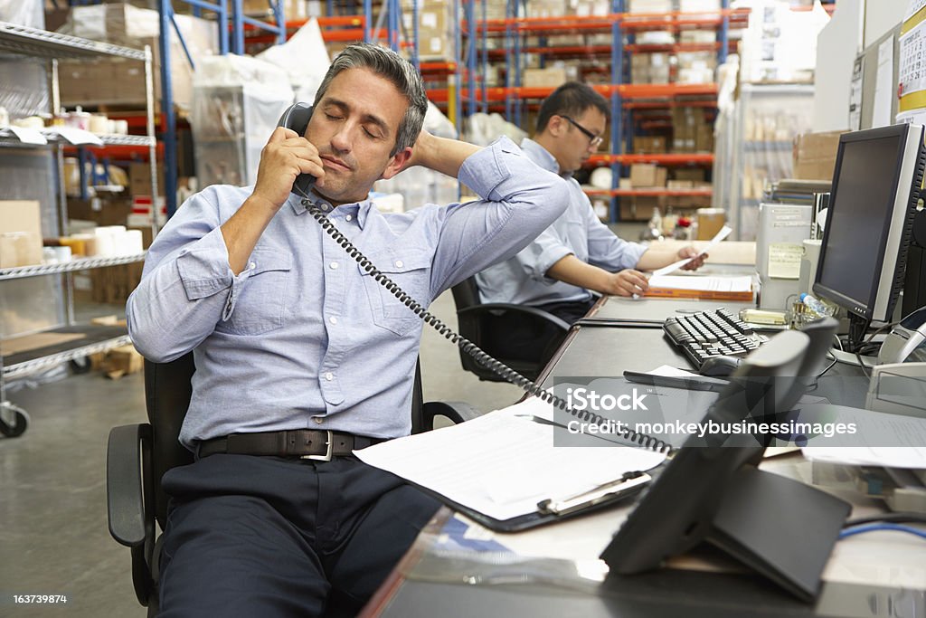 Businessman taking phone call at his warehouse desk Two Businessmen Working At Desk In Warehouse Owner Stock Photo