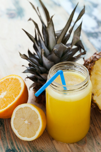 Fresh squeezed orange,lemon and pineapple juice arranged with full and cut fruits on wooden rustic table. Shallow DOF