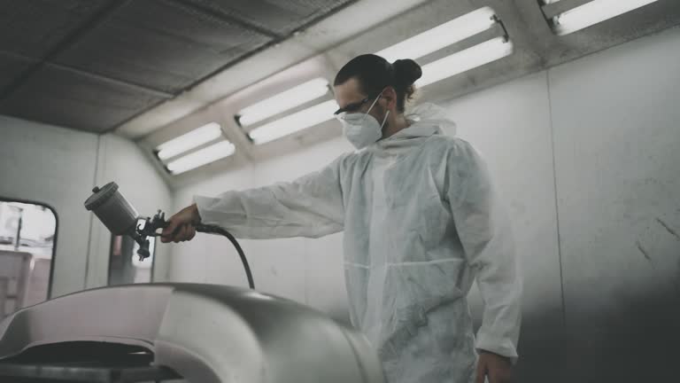 Car painter spraying primer on rear bumper.