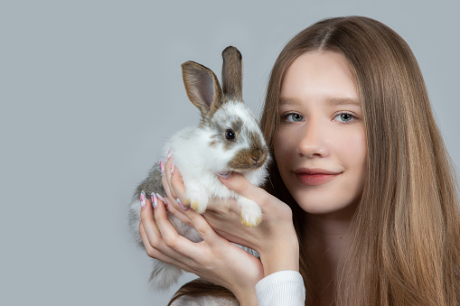 Girl holding a rabbit close-up on a gray background.