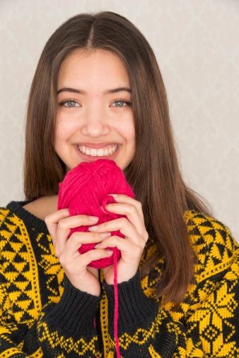 Beautiful teenage girl hold a ball of red cotton yarn used for knitting or crochet work