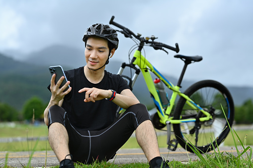 Handsome asian man cyclist taking a break resting from cycling bike in the morning and using mobile phone.