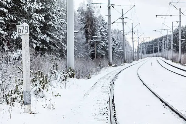 Empty electric mainline railway in winter woods with distance mark