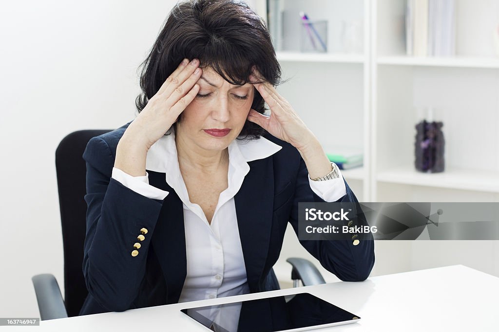 Business overworked Mature businesswoman in headache with hands on her head and  eyes closed sitting at the table. Shallow dof. Menopause Stock Photo