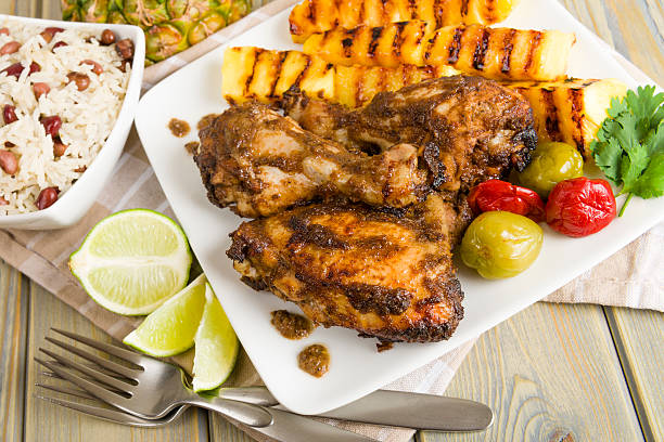 Picnic table with barbecue chicken, peppers, rice, and lemon Jerk Chicken served with pineapple, chills and rice and peas. caribbean culture stock pictures, royalty-free photos & images