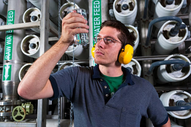 Clean Water A water technician exams a glass of water after tapping one of the filters behind him at a public water facility. public utility stock pictures, royalty-free photos & images