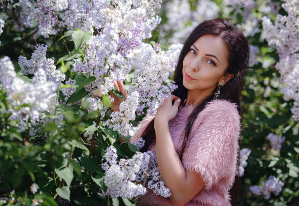 a beautiful young woman walking in a spring garden and Enjoying the Smell of Lilac. Aromatherapy and Spring Concept