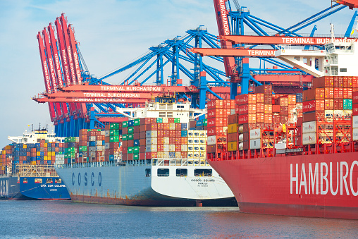 Cargo container ships with shipping containers docked at the container terminal in the port of Hamburg during a beautiful summer day.