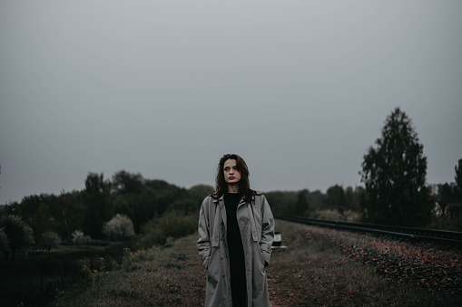 lonely woman on a cloudy day walks in a gray raincoat in nature. The concept of loneliness and existential crisis, rehabilitation.