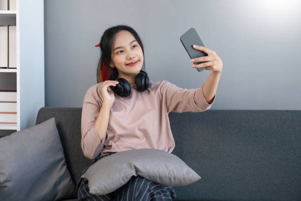 mulher sorridente nova sentada no sofá e tirando selfie - room service audio - fotografias e filmes do acervo