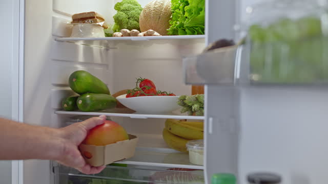 LD Male hand placing tofu and mango into the fridge