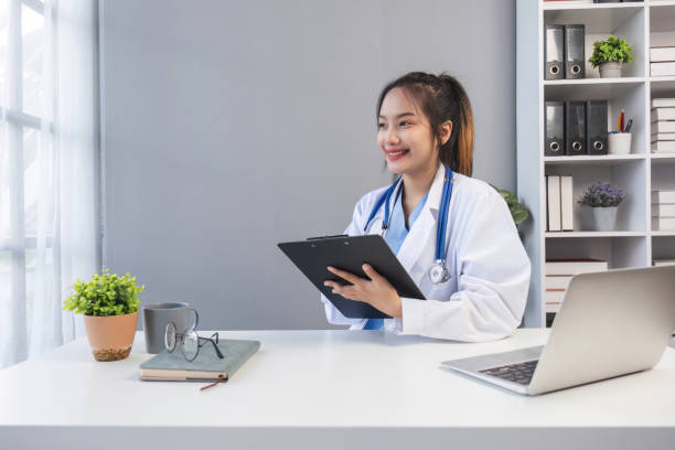istock Asian doctor young beautiful woman smiling using working with a laptop computer and her writing something on paperwork or clipboard white paper at hospital desk office, Healthcare medical concept 1637595945