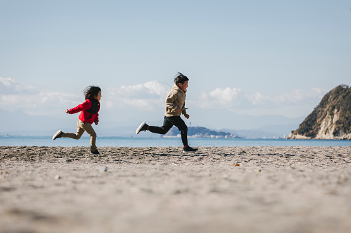 Asian sibling running in the beach.