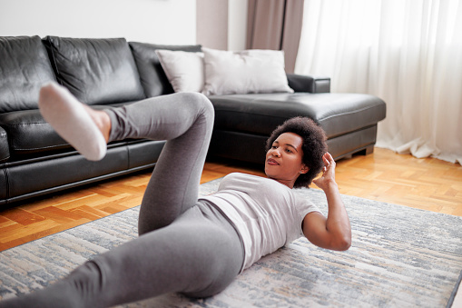 Athlete exercising sit-ups with hands behind her head at home