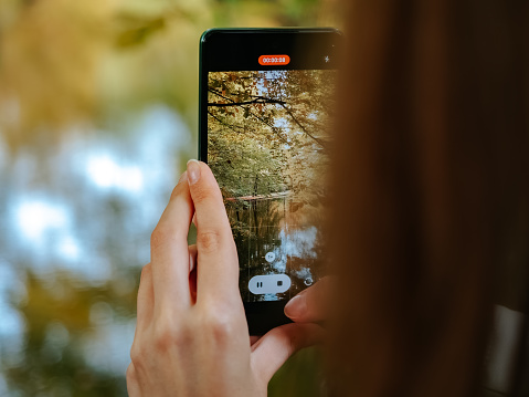 Munich, Germany - 10 10 2022: The girl shoots a video of a beautiful autumn park on a smartphone
