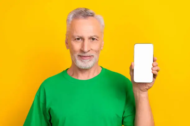 Photo of positive cool man wear green t-shirt holding apple samsung iphone device empty space isolated yellow color background.