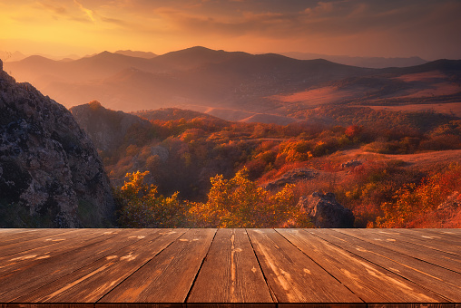 Autumn beautiful background with sunset over mountains and empty wooden table in nature outdoor. Natural template landscape.