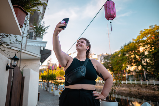 Smiling young woman walking by a lake and taking a selfie in Hanoi, Vietnam