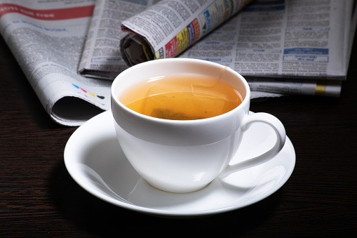 Cup of green tea with newspaper on table