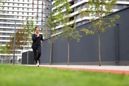 Active mature runner embraces an energetic lifestyle. Training outdoors, she exudes health and determination under the morning sun.